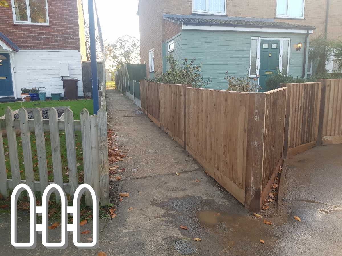 New wooden fence installed along a residential alleyway with houses and a green door in the background