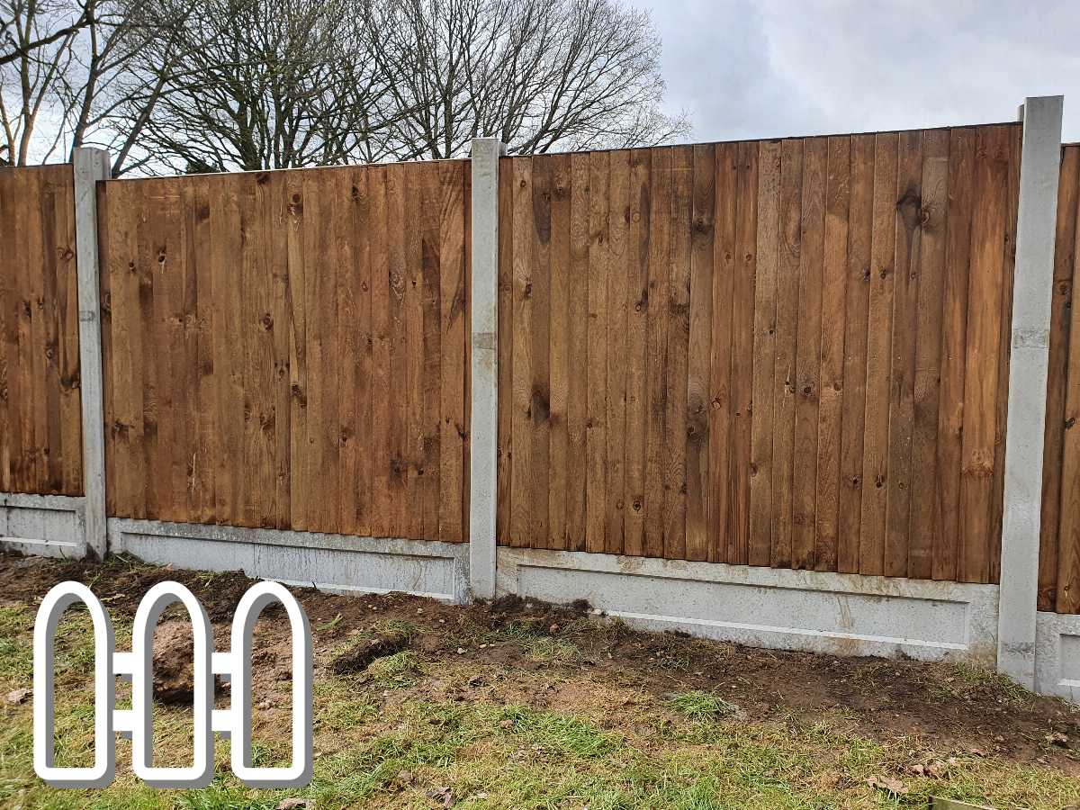 New wooden fence panels installed between concrete posts, showcasing robust and durable construction on a grassy terrain with trees in the background.