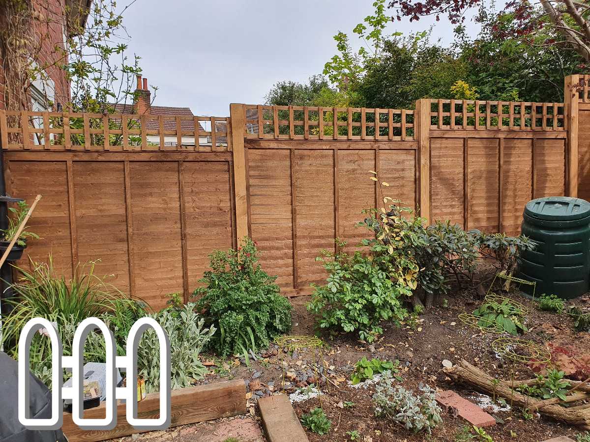 Newly installed wooden fence with lattice top in a garden, surrounded by various plants and a compost bin
